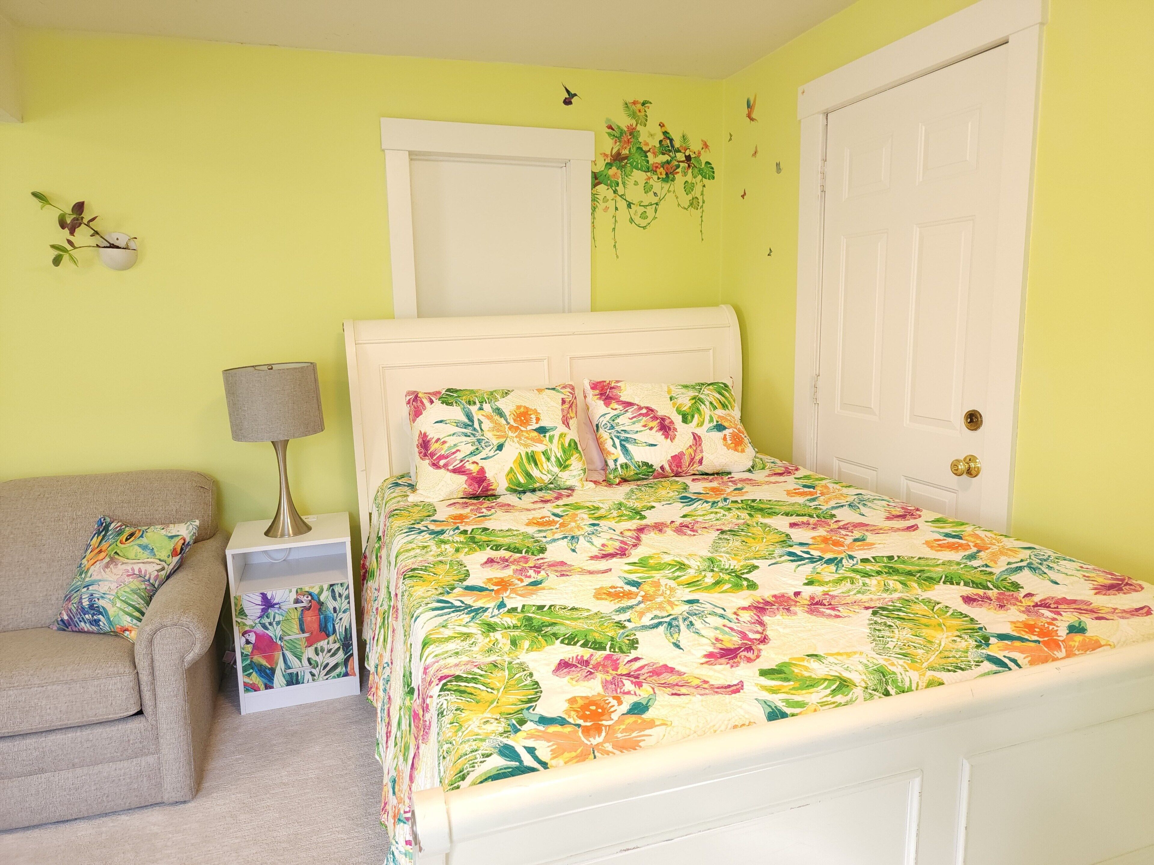 A bedroom with a bed, a nightstand, a lamp, a chair, and a door.