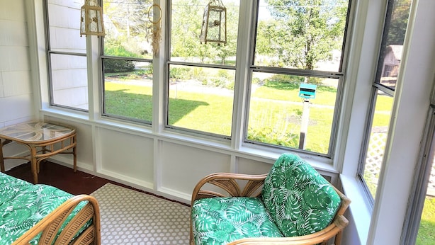Una sala de estar con mobiliario de mimbre, ventanas amplias y luces colgantes.