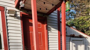 Una casa con puerta roja, un porche con escalones y una valla de madera al fondo.