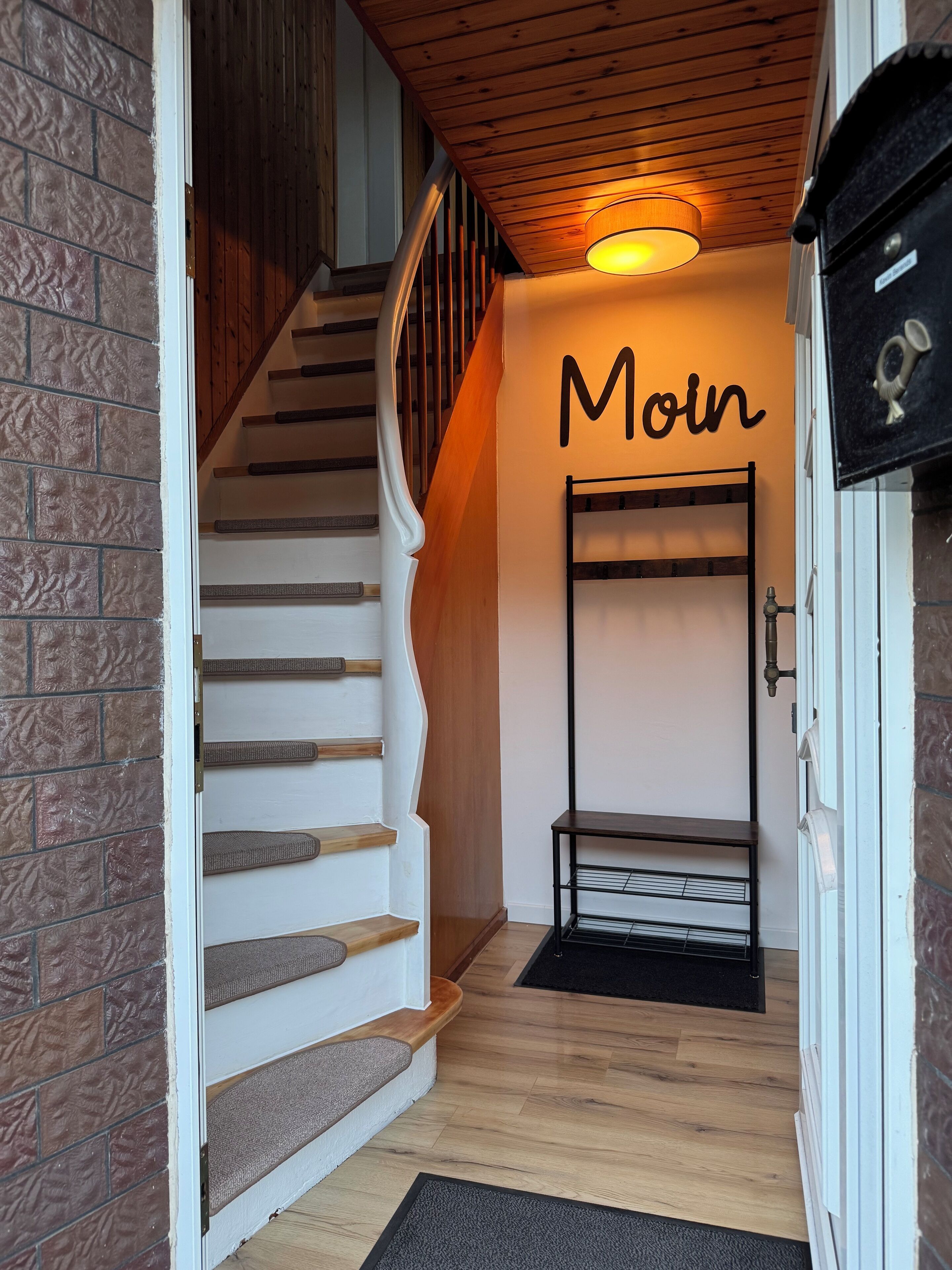 A staircase with a wooden finish, a wall-mounted light fixture, and a metal rack.