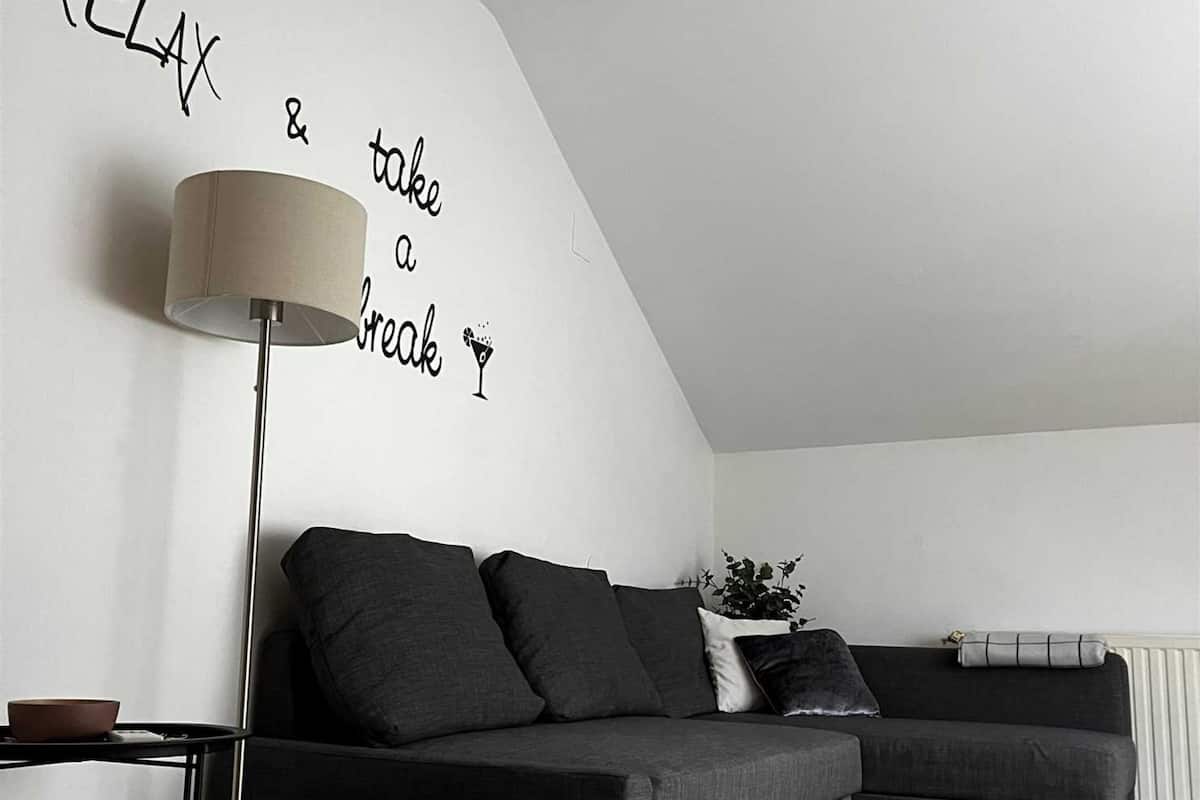 Een moderne woonkamer met een grijze bank, een vloerlamp en een muur met een motiverende quote.