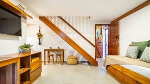 A modern bedroom with a wooden bed, a TV mounted on the wall, a desk with two chairs, and a staircase leading to another room. - ARARA HOUSE JERI (Jijoca de Jericoacoara)