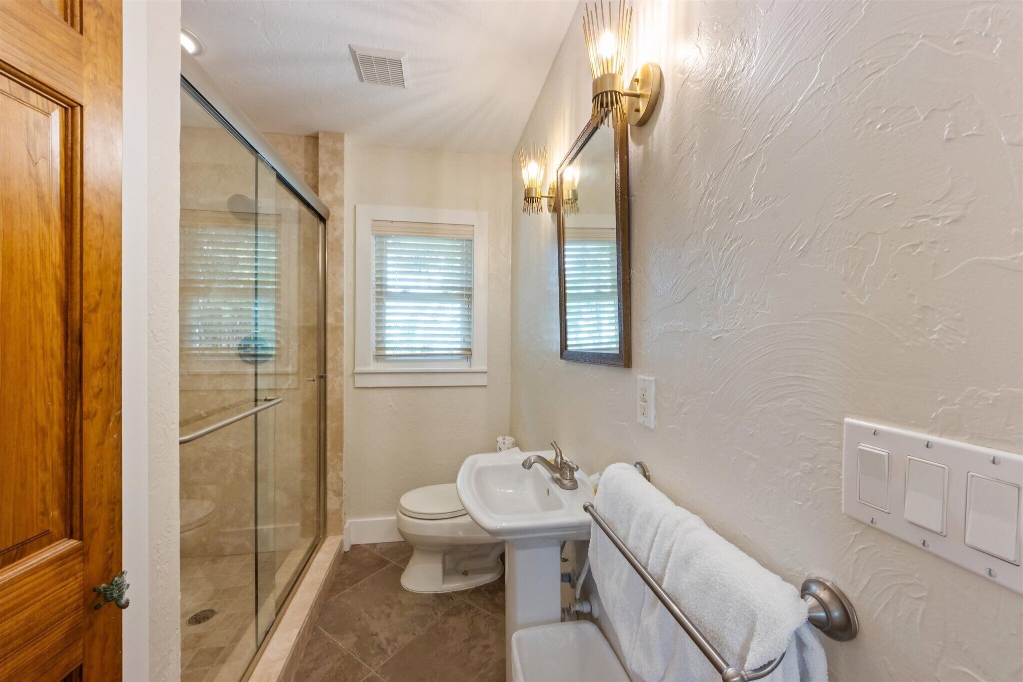 A bathroom with a glass shower enclosure, a toilet, a sink, and a towel rack.