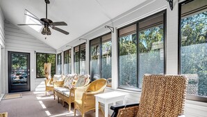 A sunlit room with wicker furniture, large windows, and a ceiling fan.