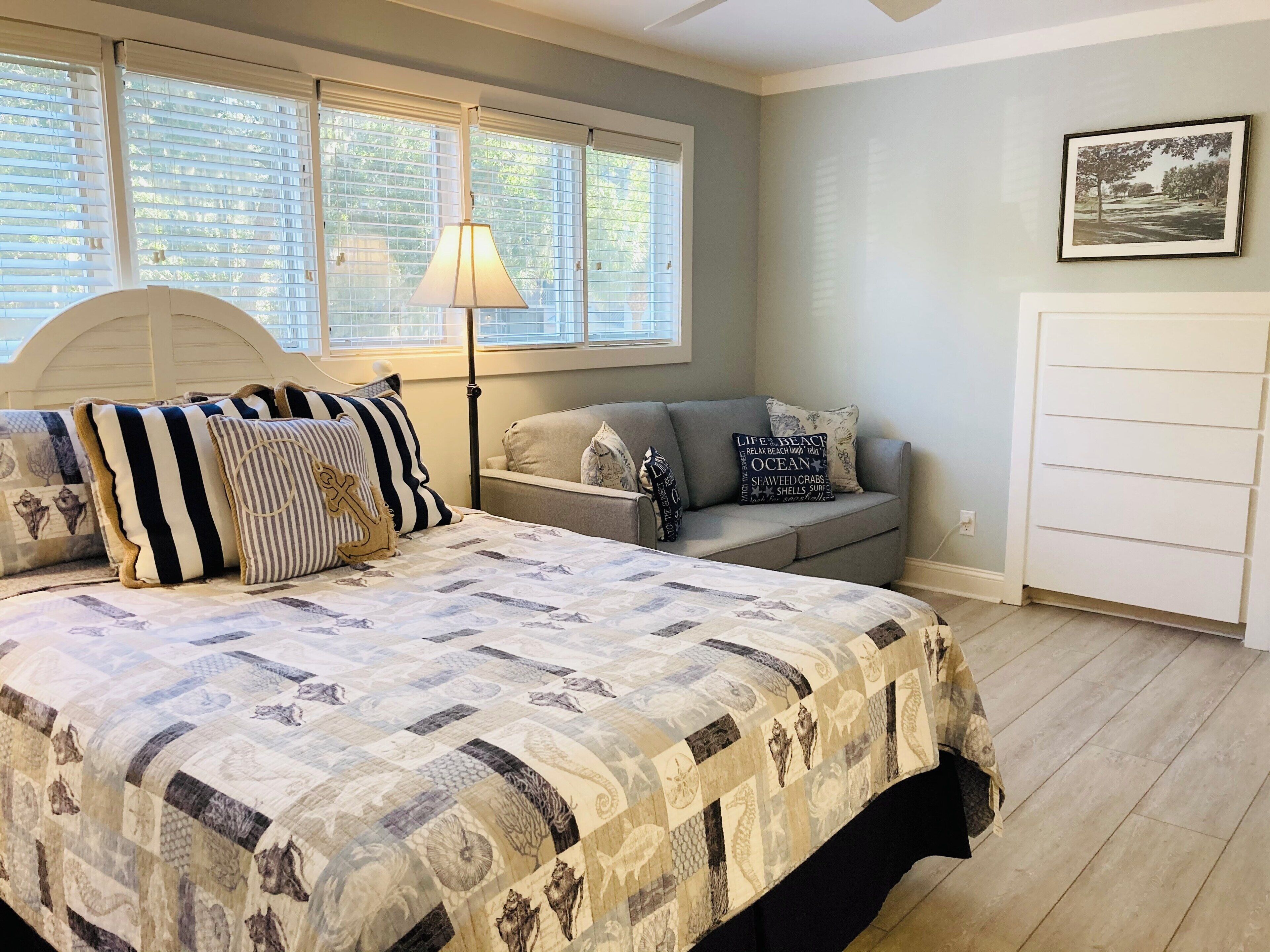 A bedroom with a bed, a sofa, a lamp, and a picture on the wall.