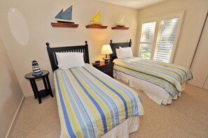 A bedroom with two beds, a nightstand, a lamp, and sailboat decorations on the wall.
