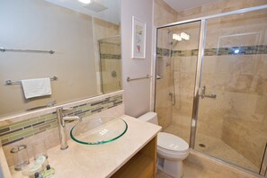 A bathroom with a glass bowl sink, a toilet, and a glass-enclosed shower.