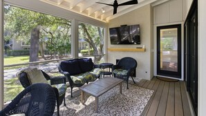 Un patio couvert avec des meubles en osier, un téléviseur à écran plat et un ventilateur de plafond.