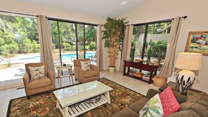 A living room with a sofa, chairs, a coffee table, and a view of a swimming pool. - 41 Deer Run Lane at The Sea Pines Resort (Hilton Head Island)