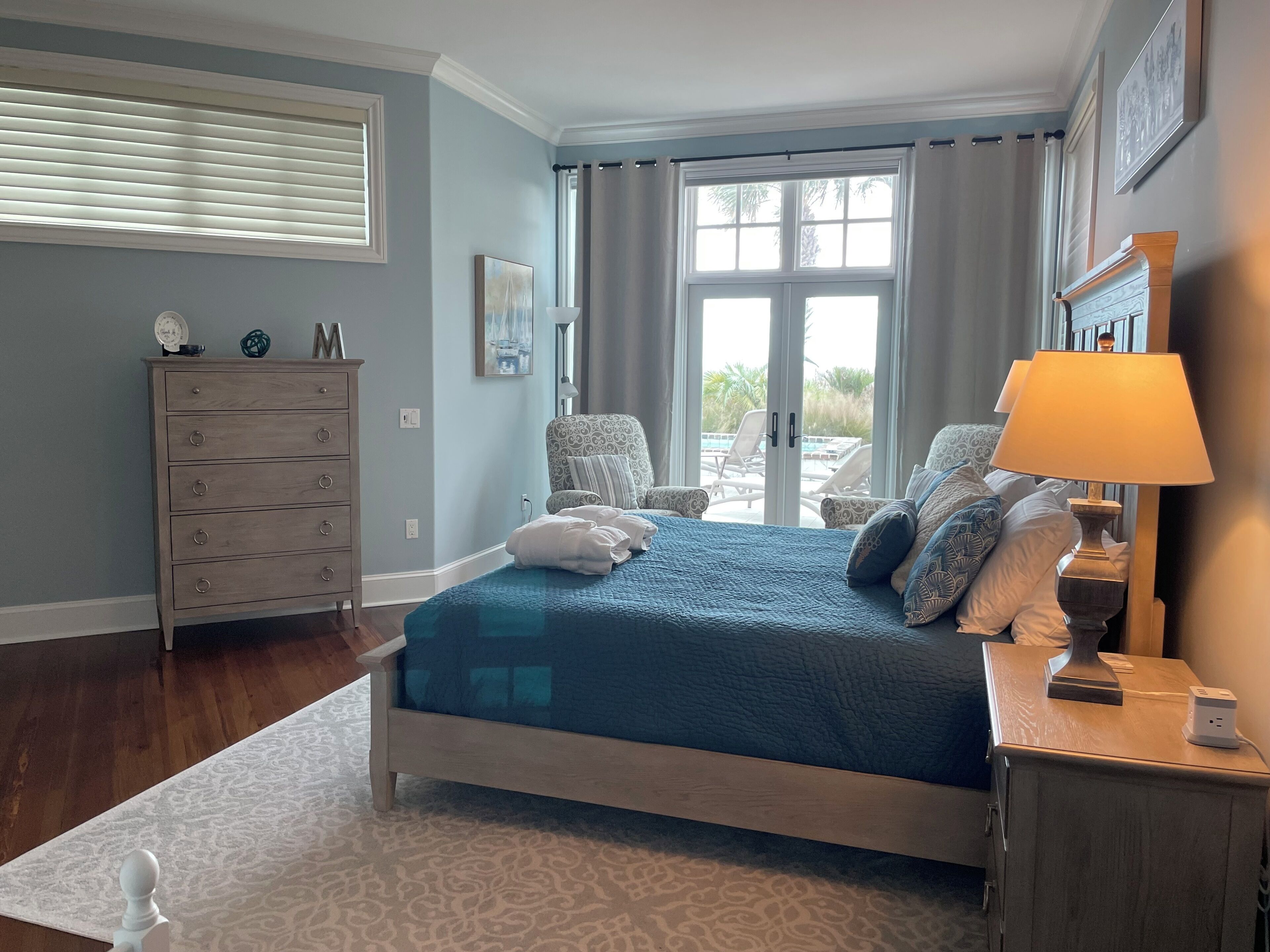 A bedroom with a bed, a dresser, a lamp, and a view of the outdoors.