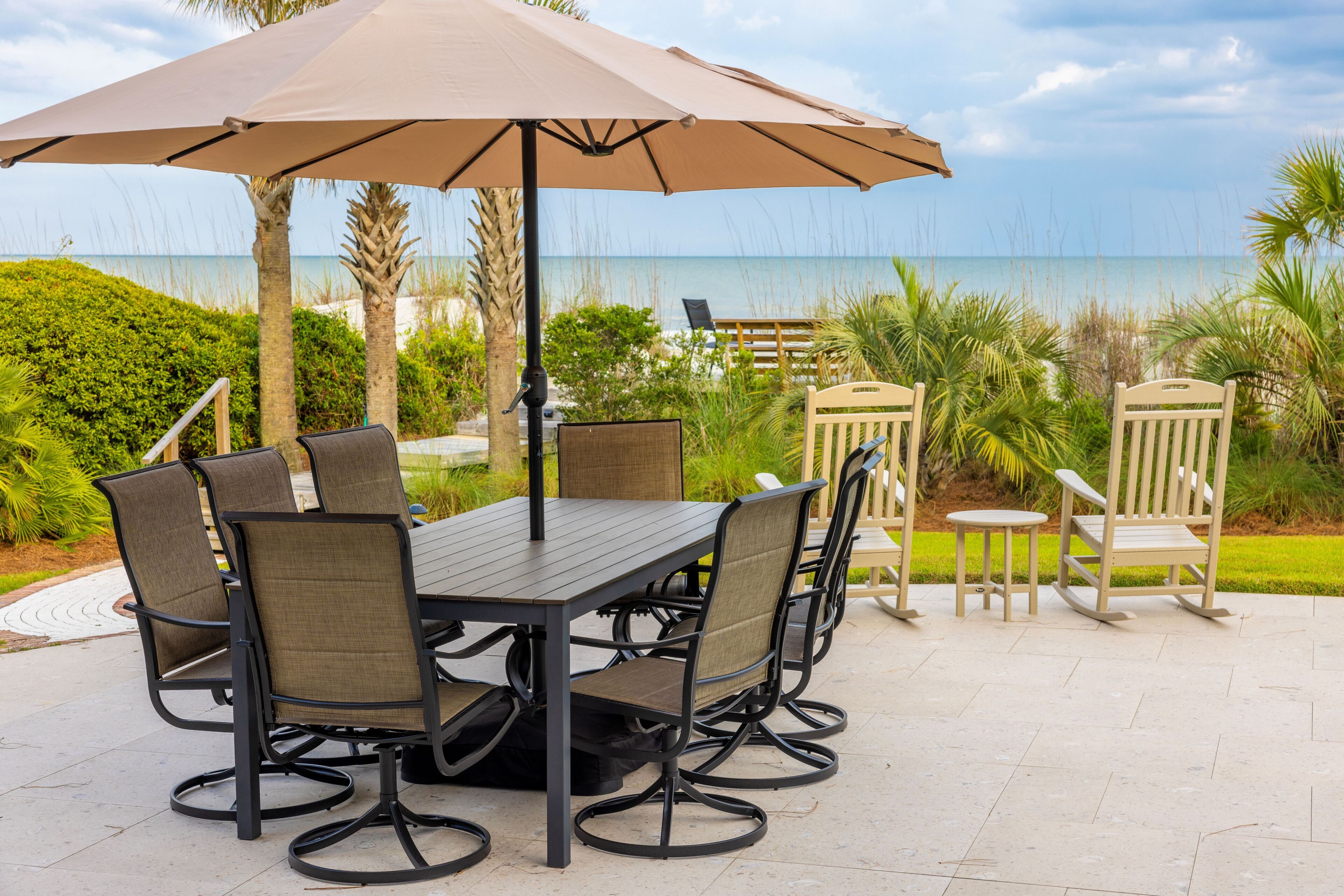 An outdoor dining area with a table and chairs, a large umbrella, and a view of the ocean.