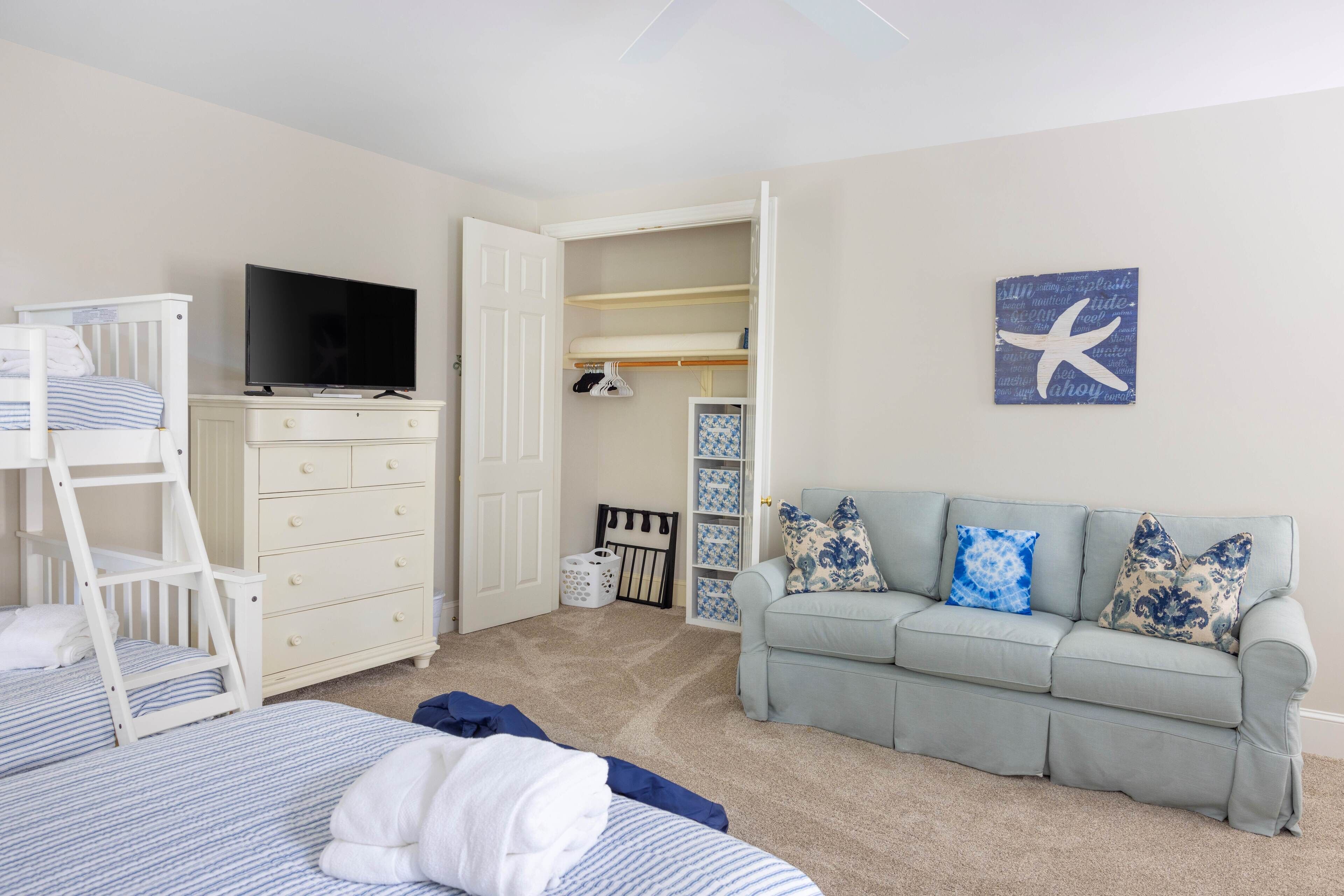 A bedroom with a bunk bed, a television on a dresser, a light blue sofa with patterned cushions, and a starfish wall art piece.