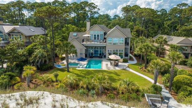 Une grande maison à deux étages avec une piscine, entourée d’une végétation luxuriante et de palmiers.