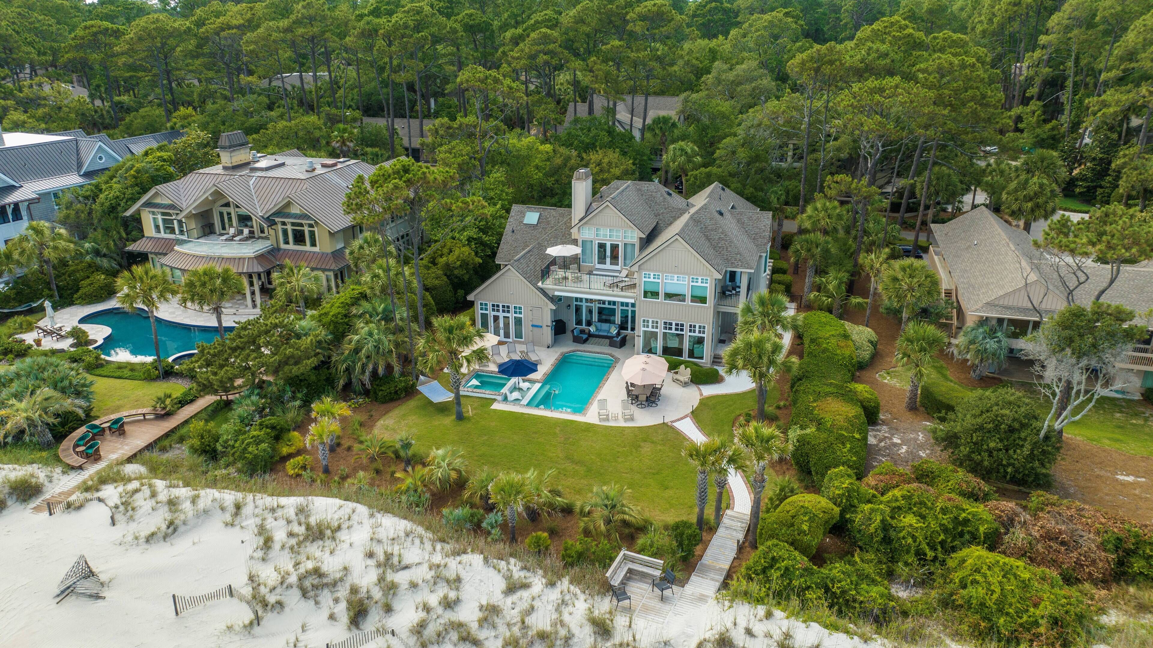 A large house with a swimming pool, surrounded by lush greenery and a sandy beach area.
