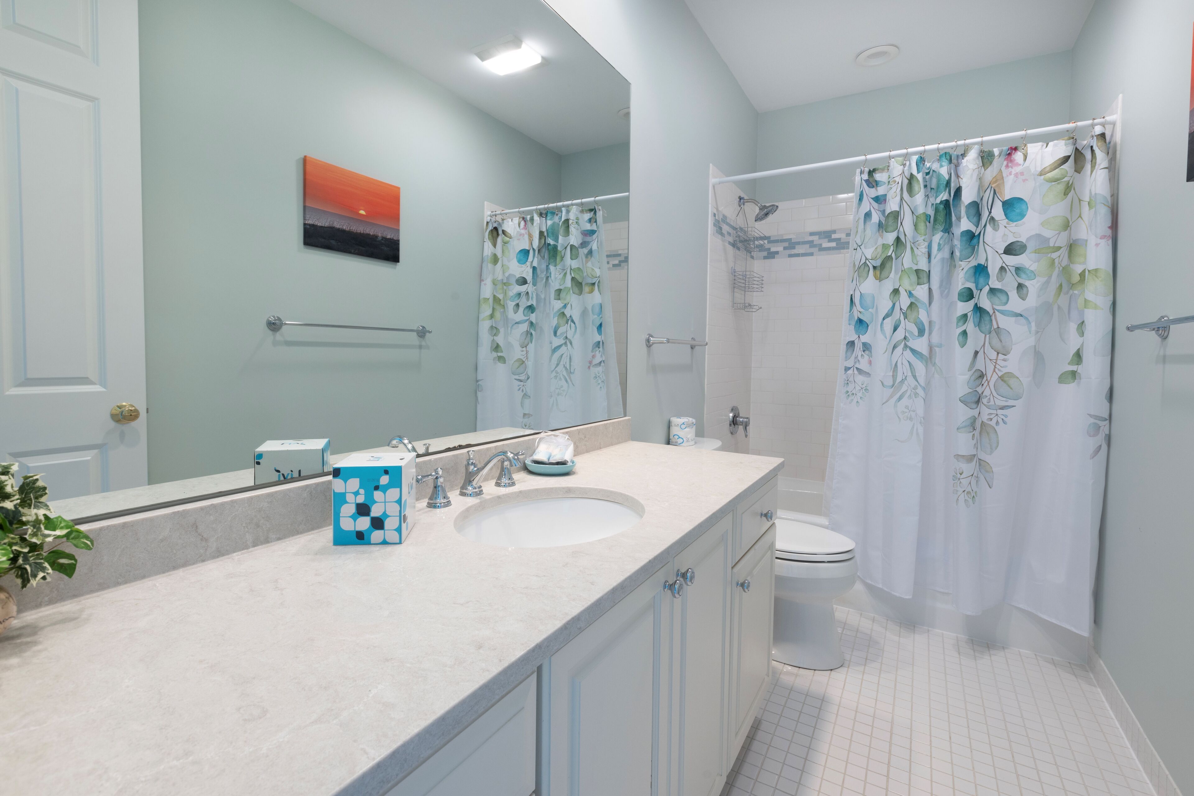 A bathroom with a large mirror, a sink, a toilet, and a shower curtain.