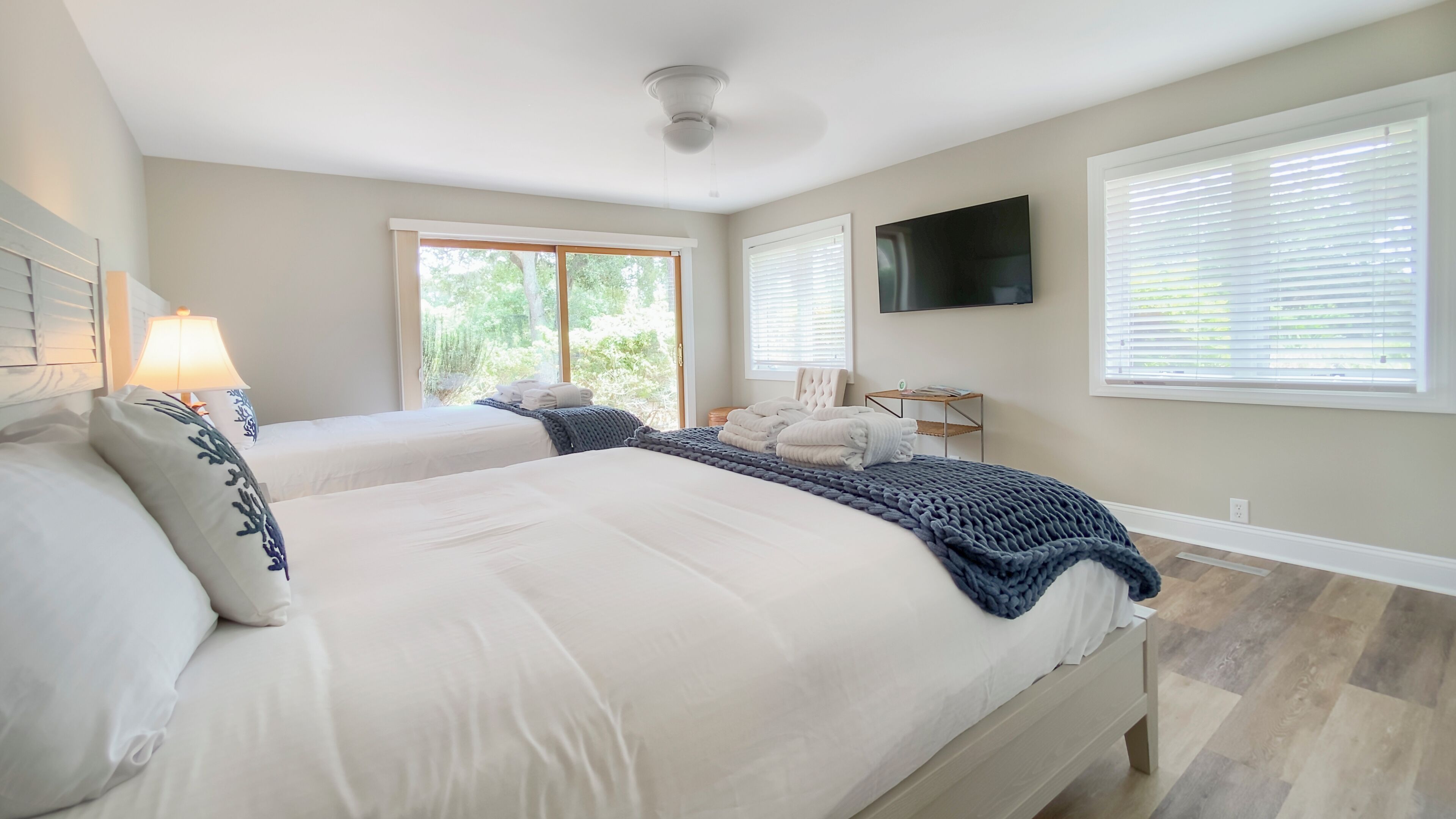 A bedroom with two beds, a TV, and a window with blinds.