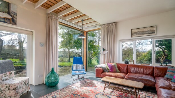 Un salon spacieux avec une grande fenêtre, un canapé en cuir marron, un fauteuil bleu et un tapis à motifs.