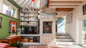 Un salon chaleureux avec une cheminée, des étagères à livres, un tapis rouge à motifs et un escalier menant à un autre niveau.