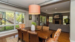 A dining area with a wooden table, wicker chairs, and a large hanging light fixture. - Juniper Presents: The Vineyard Loft - Cool Harbert Loft Near Beach with Fire Pit (Harbert)