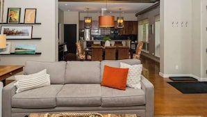 A living room with a sofa, a coffee table, and a kitchen in the background. - Juniper Presents: The Vineyard Loft - Cool Harbert Loft Near Beach with Fire Pit (Harbert)