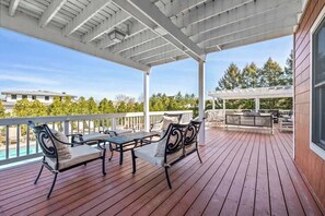 A wooden deck with outdoor furniture, a pergola, and a view of a swimming pool and buildings. - Juniper Presents: Sunny Dunes Retreat - Pool, Hot Tub & Golf Carts (Grand Beach)