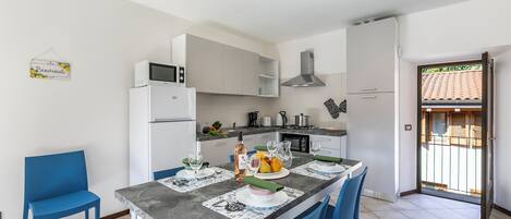 Una cocina moderna con armarios blancos, un microondas integrado y una zona de comedor con sillas azules y una mesa de mármol.