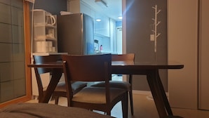 A compact room with a wooden dining table and chairs, a kitchenette area, and a view of the adjacent room.