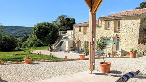 A covered outdoor seating area with two striped lounge chairs, a stone building in the background, and a gravel pathway leading to a staircase. - Mas d'Eyrolles (Sainte-Anastasie)