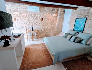 A bedroom with a stone wall, a bed, a desk with a TV, a chair, and a window. - Mas d'Eyrolles (Sainte-Anastasie)