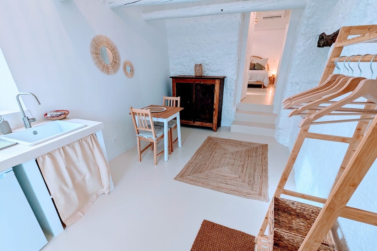 Una cocina compacta con un lavamanos, sillas de madera, una mesa de comedor y una escalera que lleva a un dormitorio.