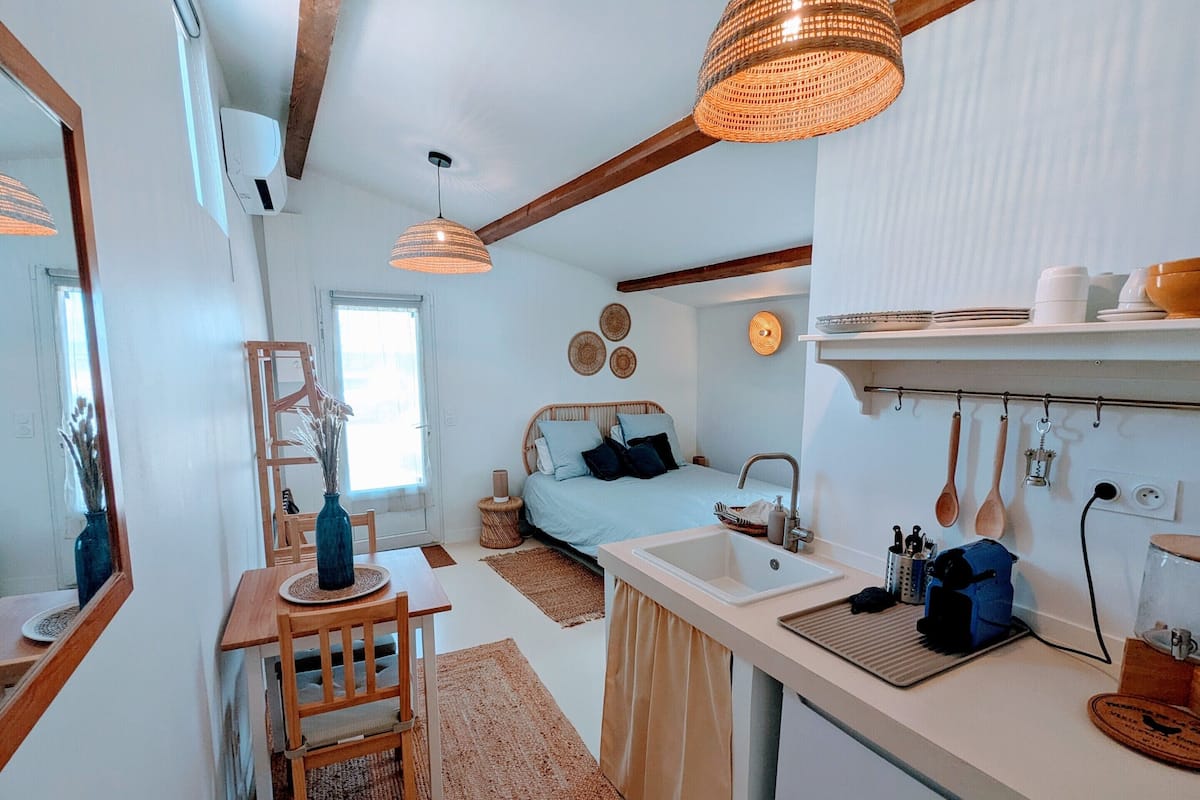 Una habitación pequeña y bien iluminada con cama, escritorio, lavabo y espejo.