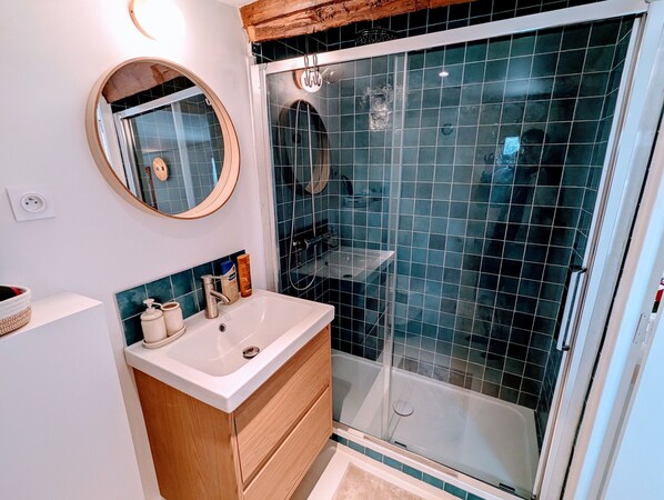 Un baño moderno con un lavamanos blanco, tocador de madera y cabina de ducha de vidrio.