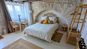 A bedroom with a stone wall, a bed with a wooden headboard, a small table with chairs, and a hanging rack. - Mas d'Eyrolles (Sainte-Anastasie)