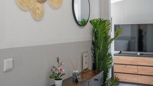 A modern living room with a wooden cabinet, a large mirror, decorative wall art, a potted orchid, and a television.