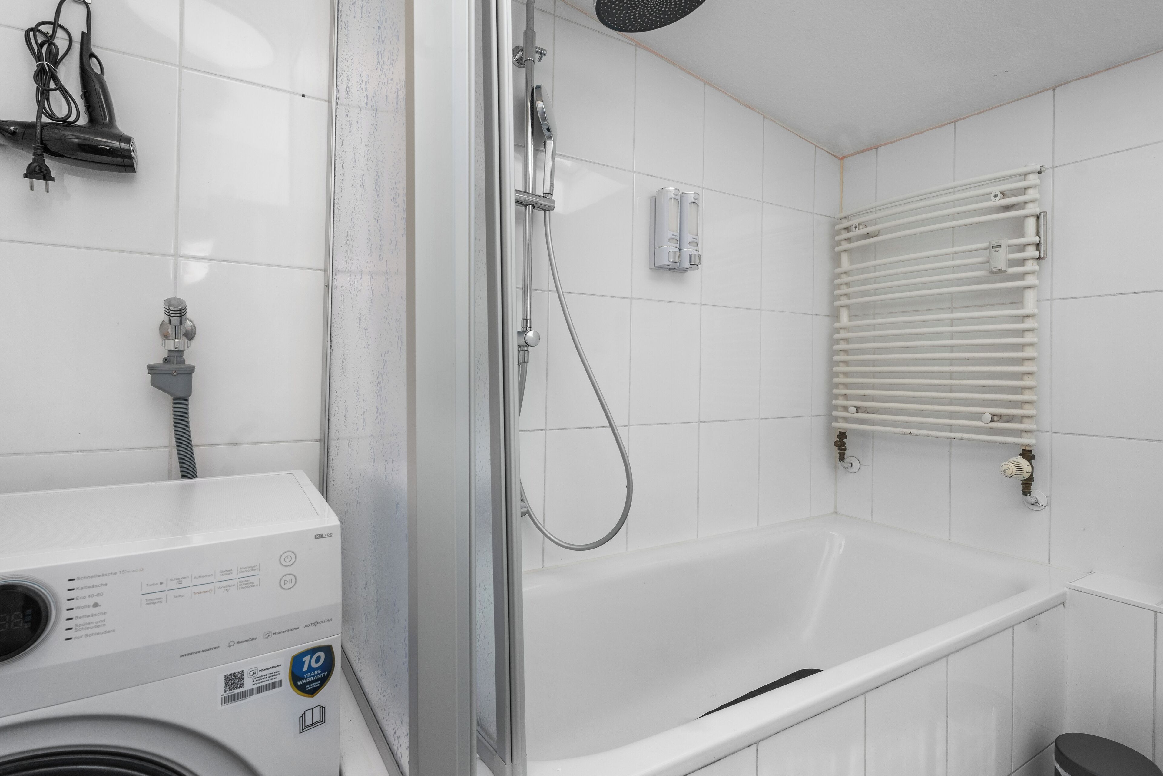 Un baño moderno con una bañera blanca, cabina de ducha con mampara de vidrio y calefacción integrada.