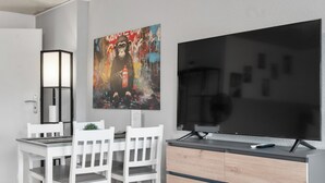 A modern kitchen with a dining area, a large flat-screen TV, and a colorful abstract painting on the wall.
