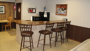 A bar area with a wooden counter, three stools, a refrigerator, and a 'No Smoking' sign.