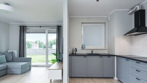 A modern kitchen with grey cabinets, a black range hood, and a window with blinds. - Wałowa - Garden View by Grand Apartments (Gdansk)