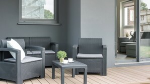 A modern outdoor seating area with wicker furniture and a small table with cups and a plant. - Wałowa - Garden View by Grand Apartments (Gdansk)