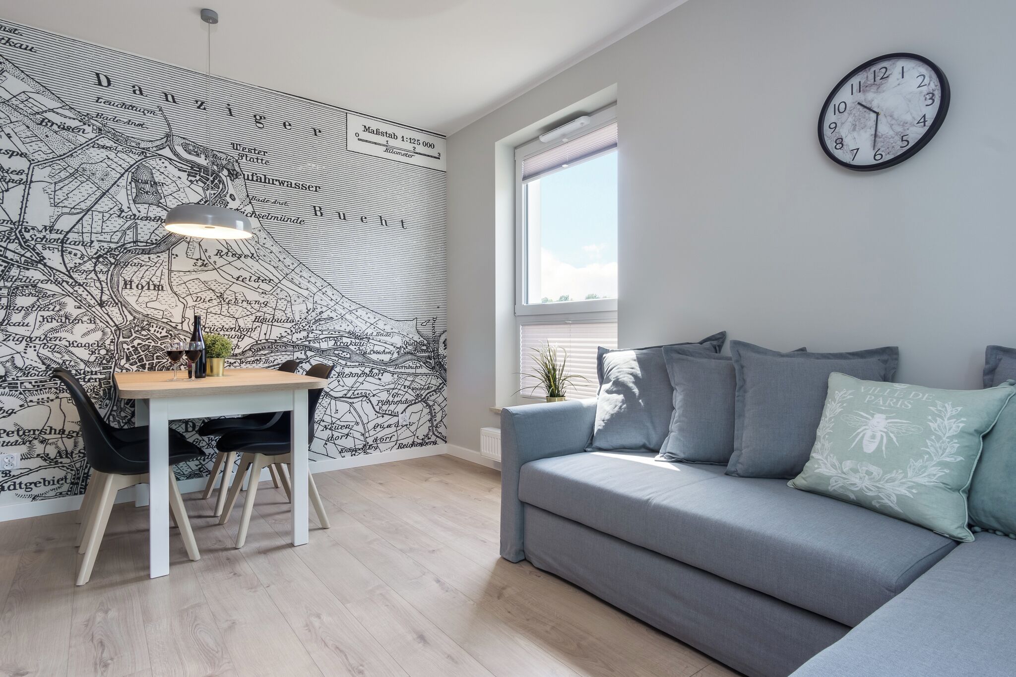 A modern living room with a dining area, featuring a map wall, a sofa, a clock, and a window.