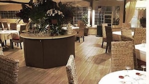 A restaurant with round tables, wicker chairs, and a central plant display. - Portorosa Beach Resort (Tonnarella)