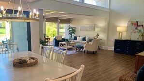 Ampla sala de estar com mesa de jantar, cadeiras e sofá. Uma grande janela oferece luz natural e vista para o exterior.