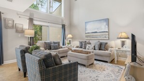 A living room with a sofa set, a coffee table, a TV, and a painting on the wall. - 250 Stoney Creek Villa at The Sea Pines Resort (Hilton Head Island)