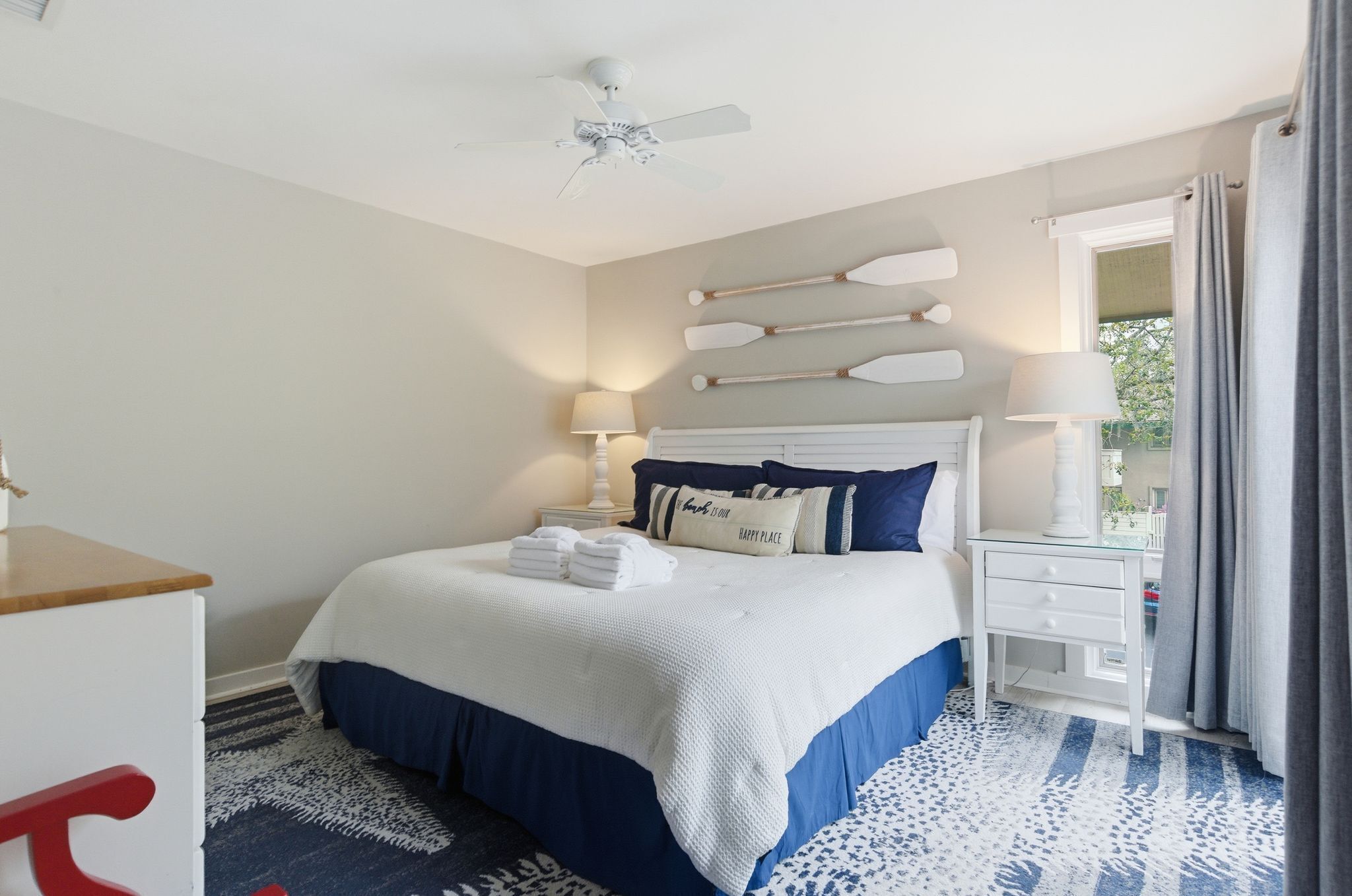 A hotel room with a bed, bedside tables, a ceiling fan, and a window with curtains.