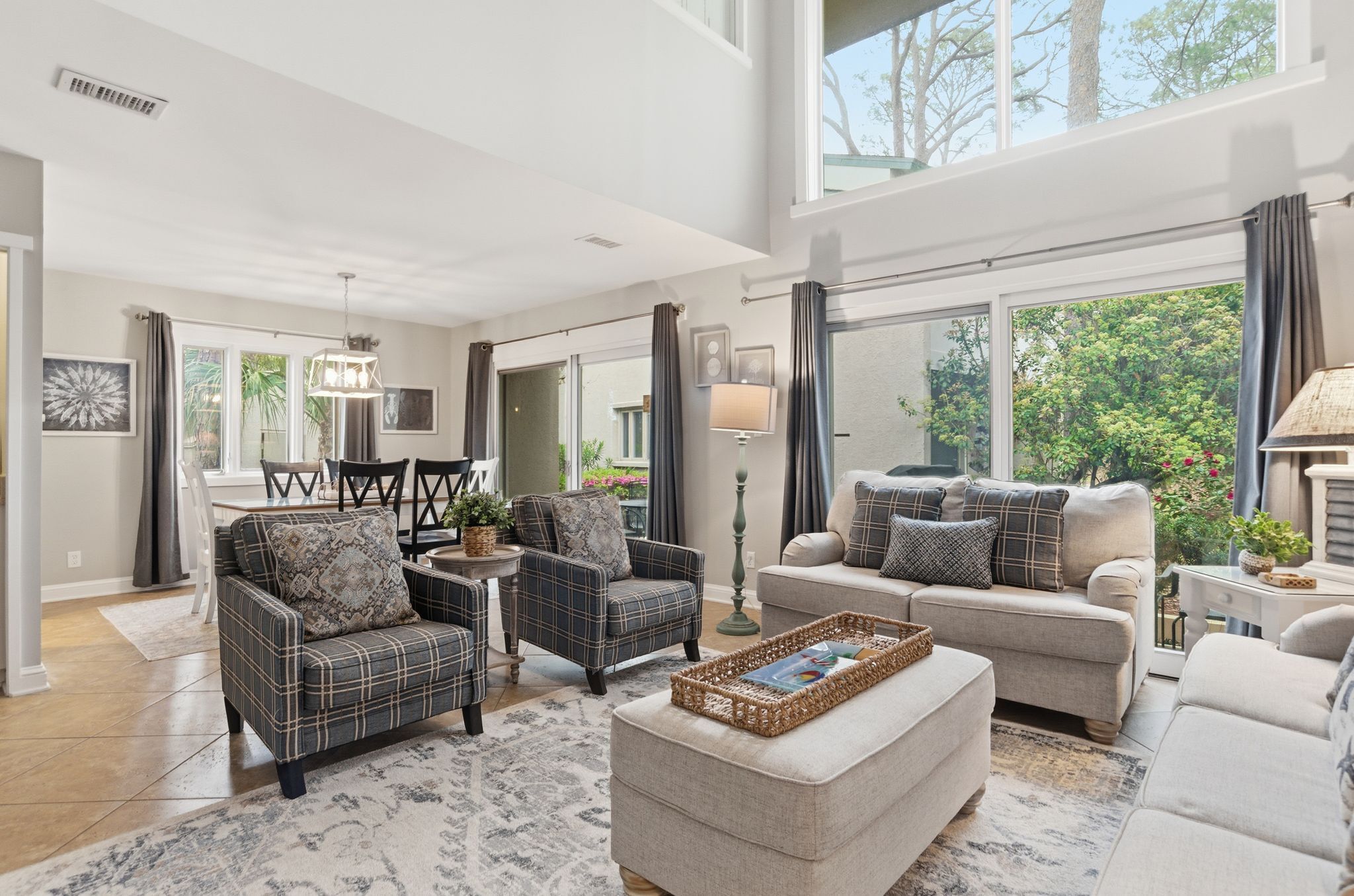 A spacious living room with a high ceiling, large windows, and a view of greenery outside.