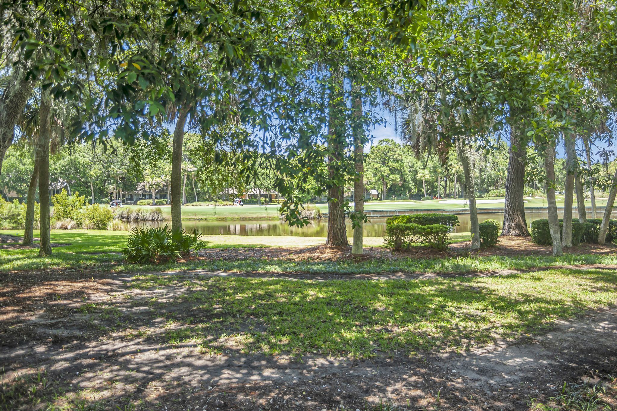 Un parque con un estanque, árboles y un campo de golf al fondo.