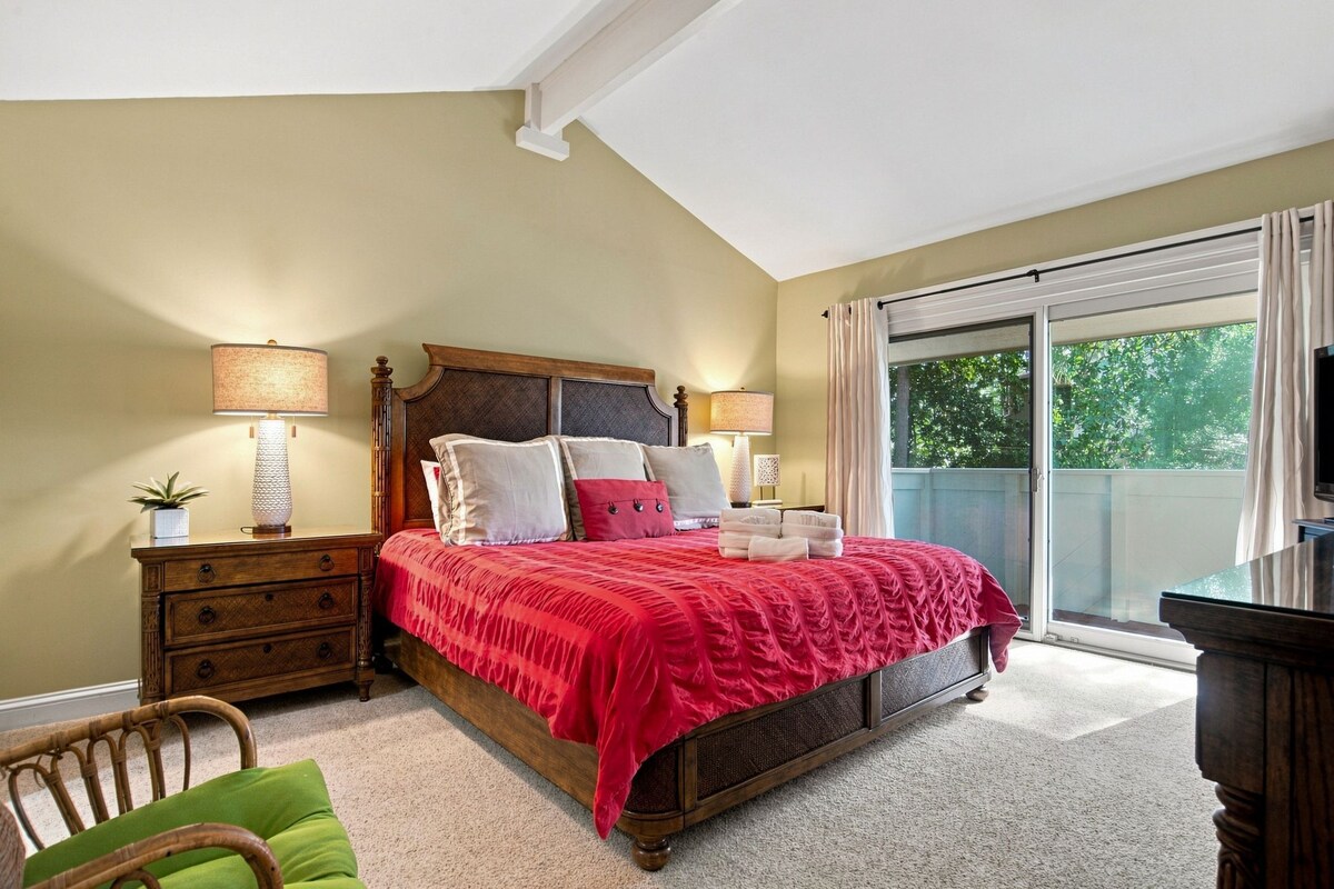 A bedroom with a large bed, two bedside tables, a chair, and a television.