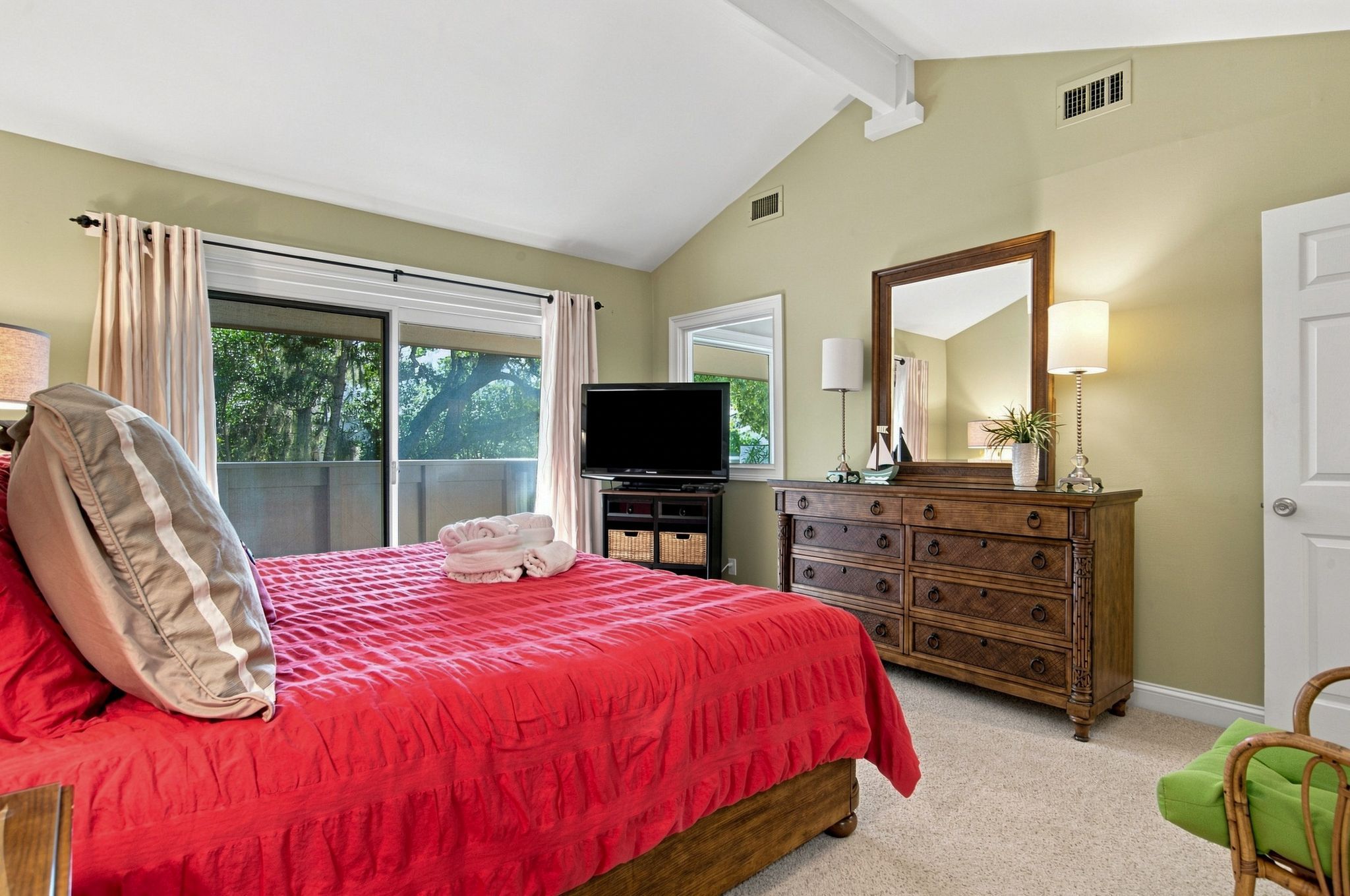 A bedroom with a bed, a dresser, a television, and a window with curtains.
