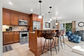 A modern kitchen with wooden cabinets, stainless steel appliances, and a bar area with stools.