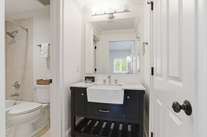 A bathroom with a white toilet, a shower, a sink with a mirror, and a towel rack. - 201 Turtle Lane at The Sea Pines Resort (Hilton Head Island)